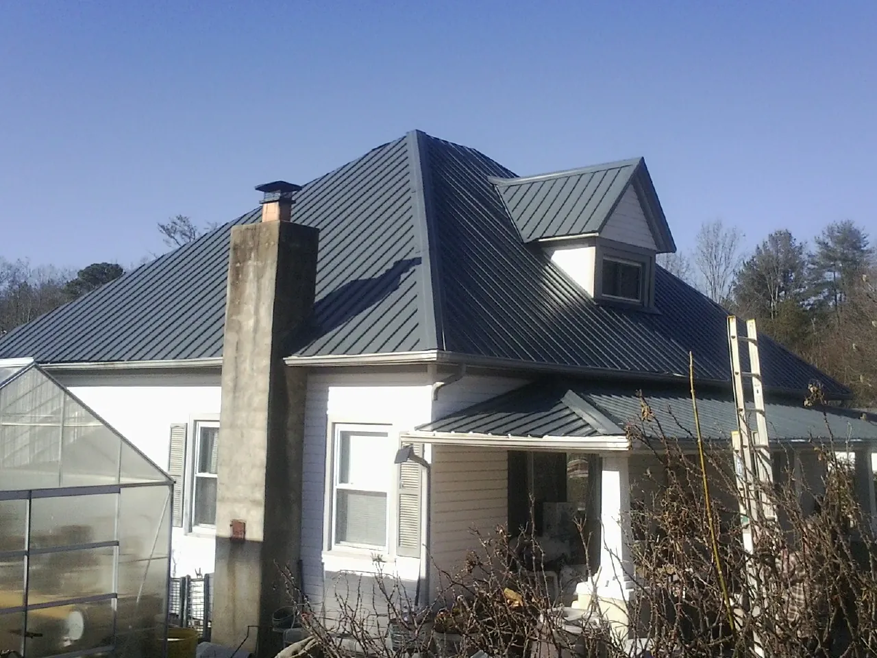 Dark blue standing seam metal roof on a white farmhouse with dormer — Slate & Tile Roof Repair by Roofing Brothers in Malinta