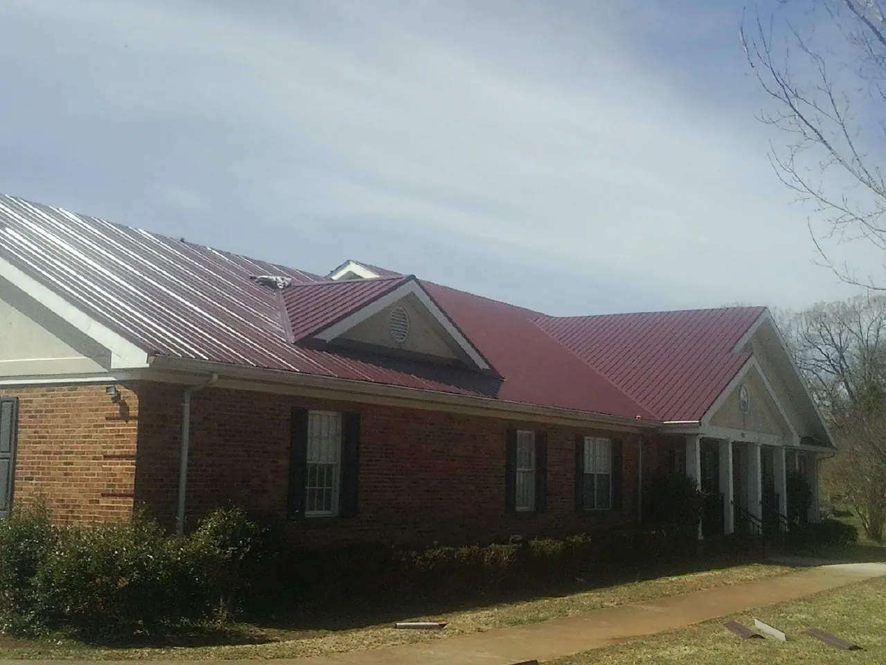 Red metal roof with gabled entries on a long brick building, from a Hail Damage Roof Repair job in Malinta