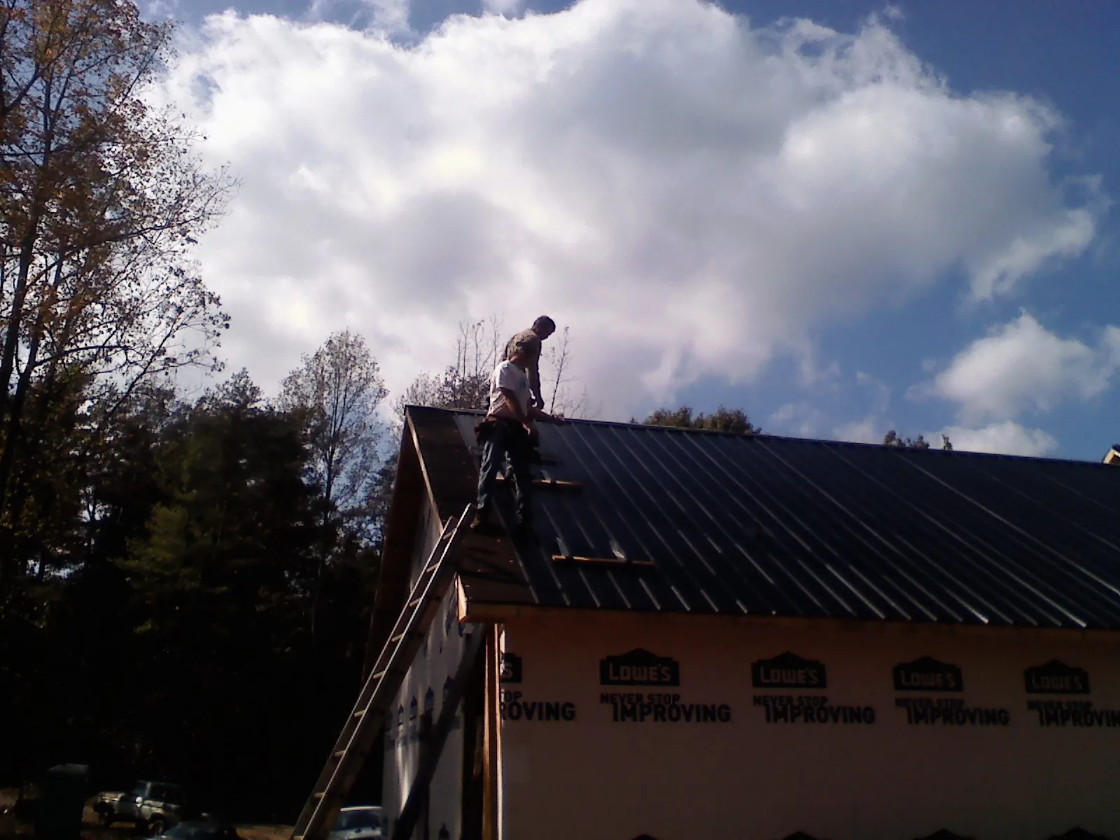 Roofer fastening dark metal panels high against a cloudy sky, from a Roof Inspection job in Malinta